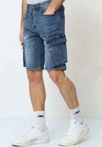 Shorts cargo en denim bleu moyen avec un look usé. Comprend plusieurs poches, une coupe longueur genou et un ourlet effiloché.