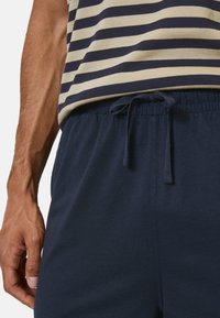 Shorts bleu marine avec une taille élastique et un cordon de serrage. Associés à une chemise rayée beige et bleu marine. Tissu en coton, texture lisse.