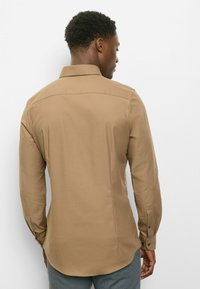 Braunes Langarmhemd mit Standardkragen, Knopfmanschetten und glatter Textur. Verfügt über einen abgerundeten Saum und einen Rückenteil mit Passe.