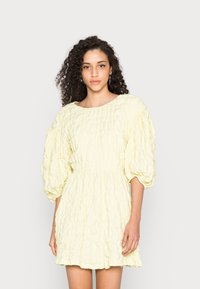 Vestido mini amarelo, texturizado, com cintura franzida, decote redondo e mangas bufantes. Tecido suave com um padrão de pregas subtil.