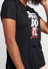 Svart T-shirt med korta ärmar i mjukt tyg, med fet vit och röd text "JUST DO YOU!" på framsidan.