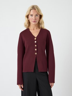 Bourgogne cardigan med V-hals, lange ermer, og fem gullknapper foran. Materialet har en jevn tekstur. Splittet kanten design.