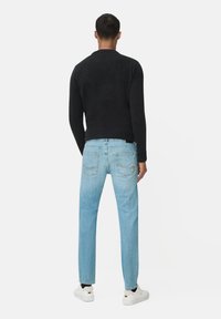 Czarny sweter dzianinowy z prążkowanym dekoltem, w połączeniu z jasnoniebieskimi spodniami o prostym kroju. Białe trampki podkreślają swobodny wygląd.