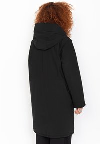 Sort hættejakke med lang, lige pasform, der har et glat ydre stof og store, funktionelle lommer.