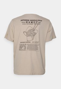 T-shirt beige avec un imprimé graphique noir représentant des ramen dans une boîte à emporter, des baguettes et des détails de restaurant dans différentes polices et tailles.