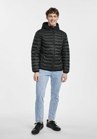 Czarna kurtka puchowa z kapturem, zapinana na zamek, z kieszeniami bocznymi, w połączeniu z jasnoniebieskimi dżinsami i czarnymi trampkami. Gładka tekstura z wypukłymi segmentami.