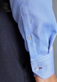 Lichtblauw overhemd met een vissengraatpatroon, knoopmanchetten en subtiele textuur. Gecombineerd met een donkerblauwe blazer.
