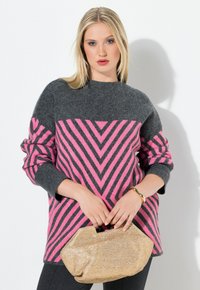Grau-rosa Chevron-musterter Strickpullover mit langen Ärmeln, kombiniert mit einer goldenen geflochtenen Handtasche und schwarzen Hosen.