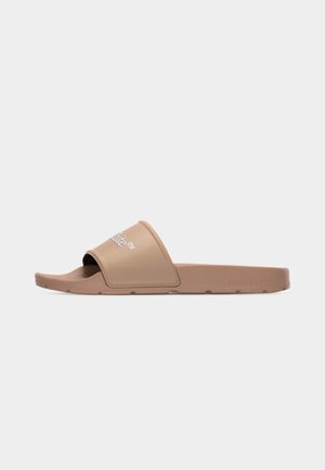 Sandalo singolo marrone chiaro con ampia fascia recante la scritta bianca "Off-White™" su uno sfondo grigio chiaro uniforme.