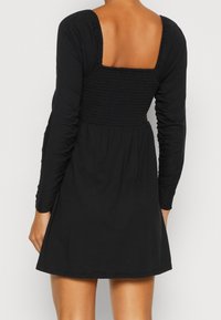 Svart klänning med långa ärmar, featuring en fyrkantig smockad rygg och en utsvängd kjol. Tillverkad av mjukt tyg med en slät textur.