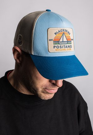 Trucker cap with a light blue front, blue visor, and beige mesh back. Features a rectangular patch with a sailboat and 'Positano Sailing Club' text.