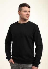 Felpa nera con colletto tondo, maniche lunghe, texture morbida, polsini a coste e orlo a costine, indossata con jeans grigio chiaro. Design semplice, senza motivi.