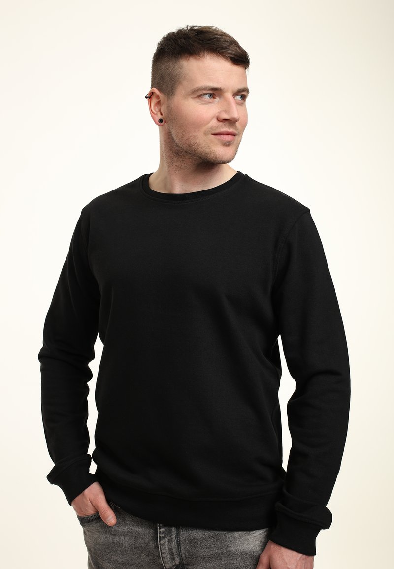 Felpa nera con colletto tondo, maniche lunghe, texture morbida, polsini a coste e orlo a costine, indossata con jeans grigio chiaro. Design semplice, senza motivi.
