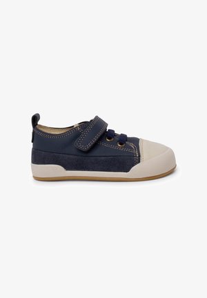 Navyblaue Turnschuhe mit einem strukturierten Textilobermaterial, einer weißen Gummizunge und einem Klettverschluss. Mit kontrastierenden Nähten und einer Gummisohle.