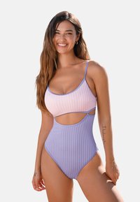 Geribbelde tankini met roze en lavendel delen, uitsnijdingen aan de zijkanten, dunne bandjes en hoge beenuitsnijding. Soepele textuur, modern ontwerp.