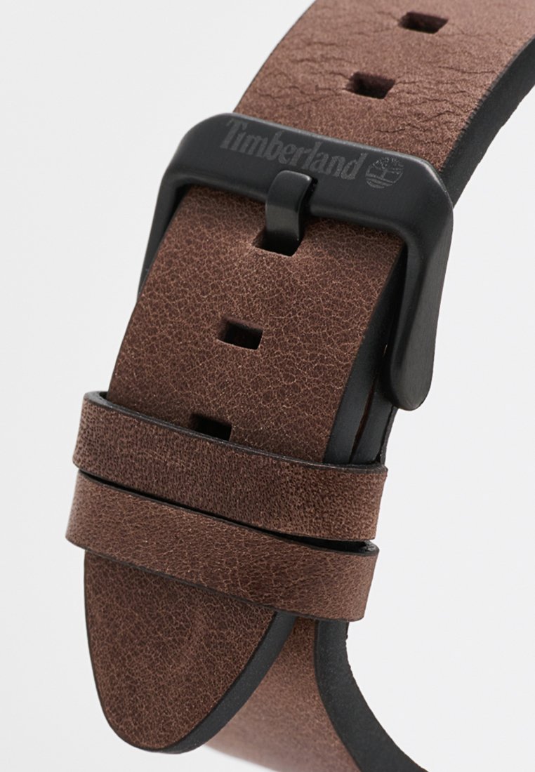 Correa de reloj de cuero marrón con un acabado texturizado, agujeros ajustables y una hebilla de metal negro con la marca Timberland.
