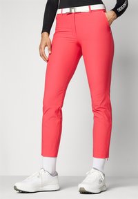 Bright pink, slim-fit pants with a smooth texture, featuring a white belt and zipper details. Worn with white sneakers and crew-length socks.