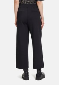 Zwarte cropped wijde broek met een gladde textuur, voorzien van twee achterzakken en een platte tailleband, gecombineerd met zwarte enkellaarsjes.