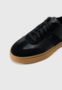 Black sneaker made of leather and suede, featuring a smooth upper, round toe, tonal laces, and a gum rubber sole.