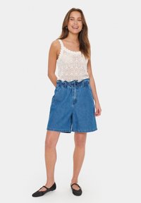 Shorts din denim cu talie înaltă și croială lejeră, având o talie cu curea și închidere cu nasturi. Top din dantelă albă cu margini ondulate.