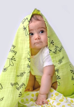 Bright green muslin blanket with black frog patterns draped over a baby. White short-sleeve onesie, yellow and white polka dot blanket below.