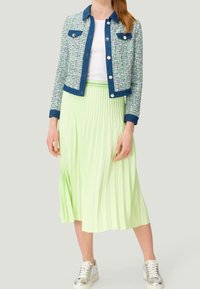 Marynarka z tweedu w kolorze niebiesko-zielonym z akcentami dżinsu, zestawiona z plisowaną spódnicą w pastelowym zielonym kolorze i srebrnymi trampkami.