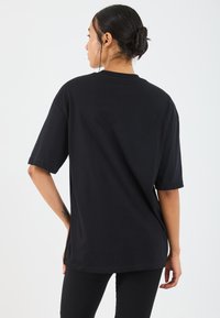 Sort oversized t-shirt med korte ærmer og rund hals, lavet af blød bomuld. Simpelt design, ingen mønstre eller hardware synlige.