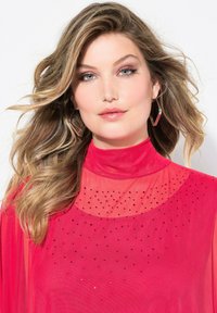 Rote transparente Bluse mit hohem Kragen, die ein gepunktetes Muster aus kleinen schwarzen und klaren Verzierungen im Brustbereich aufweist.