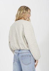Sweatshirt oversized gris clair avec ourlet côtelé et manches bouffantes, associé à un jean taille haute bleu clair. Tissu texturé doux.