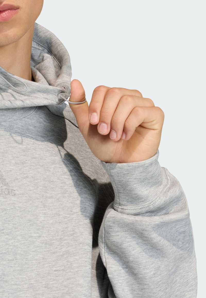 Grå hættetrøje med snøre og metalring. Stoffet har en blød tekstur, afslappet pasform og ribstrikkede manchetter.