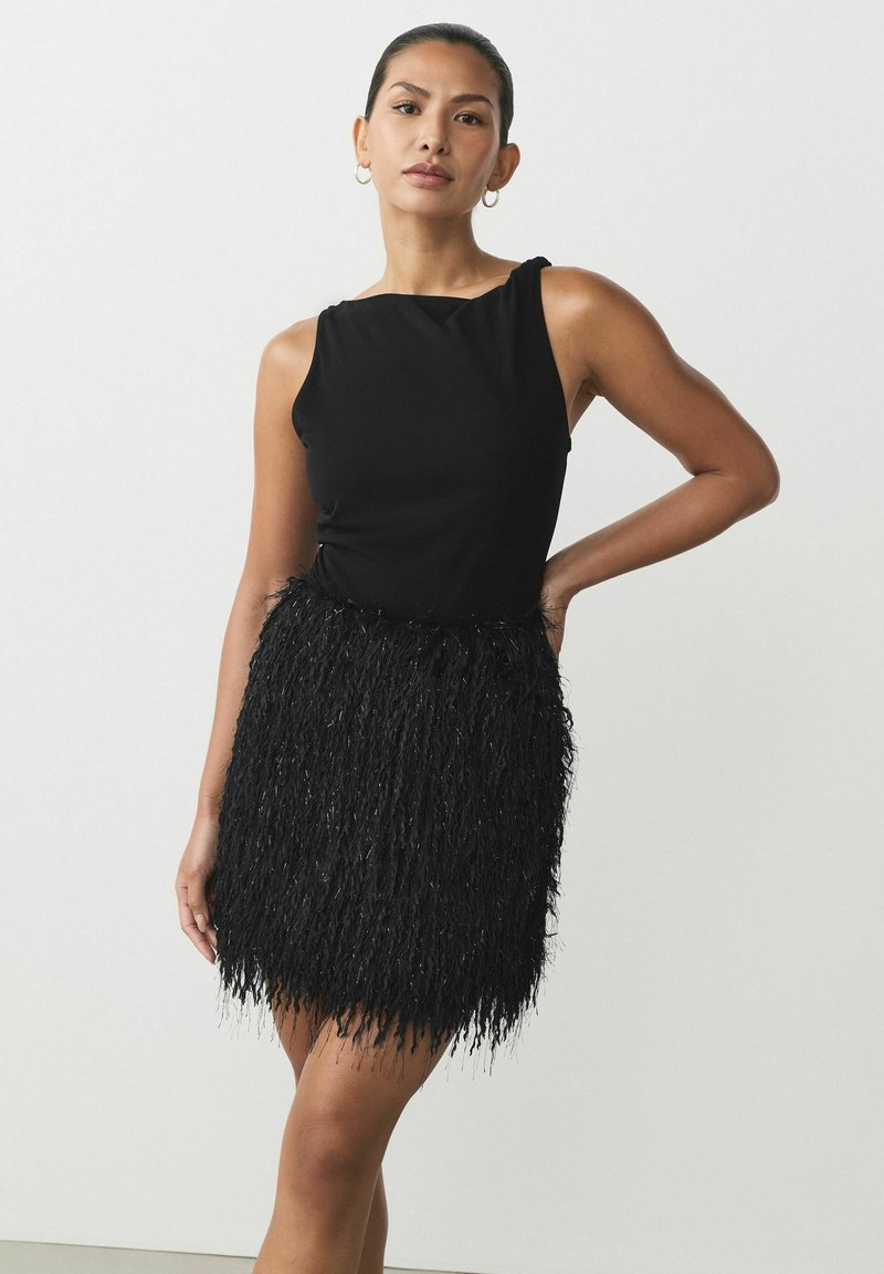 Schwarzes ärmelloses Kleid mit tailliertem Oberteil und strukturiertem Fransenrock. Der Rock verfügt über lange, glänzende Fäden für zusätzliche Dimension.