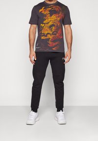 Camiseta gráfica negra con un diseño colorido de dragón, combinada con joggers negros y zapatillas blancas. La camiseta tiene mangas cortas y cuello redondo.
