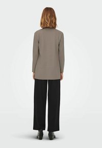Lichtgrijze lange mouw top met een getailleerde pasvorm, gecombineerd met brede zwarte broek en zwarte enkellaarsjes. Gladde stof zonder patronen.