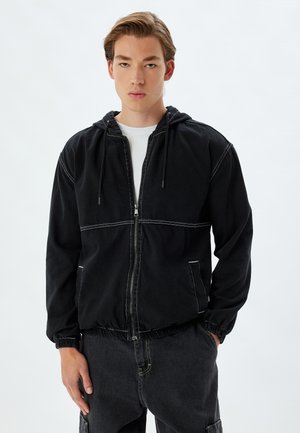 Zwarte hoodie met een ritssluiting aan de voorkant, elastische manchetten en een twee-kleurig ontwerp met witte stiksels en zijzakken. Gemaakt van denimstof.