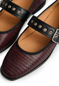Zapatos Mary Jane de cuero burdeos con un patrón de cocodrilo texturizado, correas negras con ojales de metal y un diseño de punta redonda.