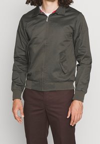 Giacca bomber verde oliva in tessuto liscio, con chiusura a zip frontale, tasca laterale, polsini a costine e dettaglio del collo a quadri.