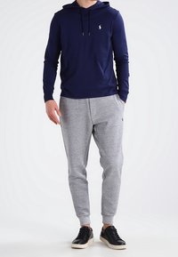 Námornícké mikiny s kapucí a dlouhým rukávem s předním logem, doplněné světle šedými zúženými tepláky a černými teniskami s krémovou podrážkou.