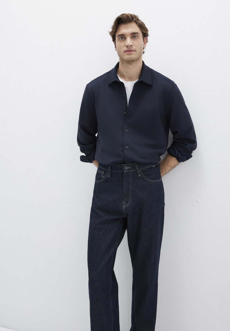 Dunkelblaues Hemd mit Knöpfen und Kragen, kombiniert mit dunkelblauen Jeans aus Denim, die über zwei vordere Taschen und sichtbare Nähte verfügen.