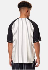 Tricou de baseball cu dungi alb-negru, cu mâneci raglan scurte; are un guler negru și accente contrastante. Textură netedă.