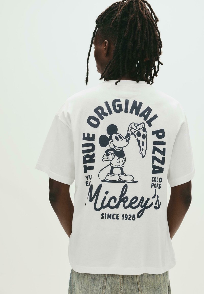 Tricou alb din bumbac, cu un imprimeu grafic al lui Mickey Mouse ținând o felie de pizza, având textul albastru "True Original Pizza" și "Mickey's."