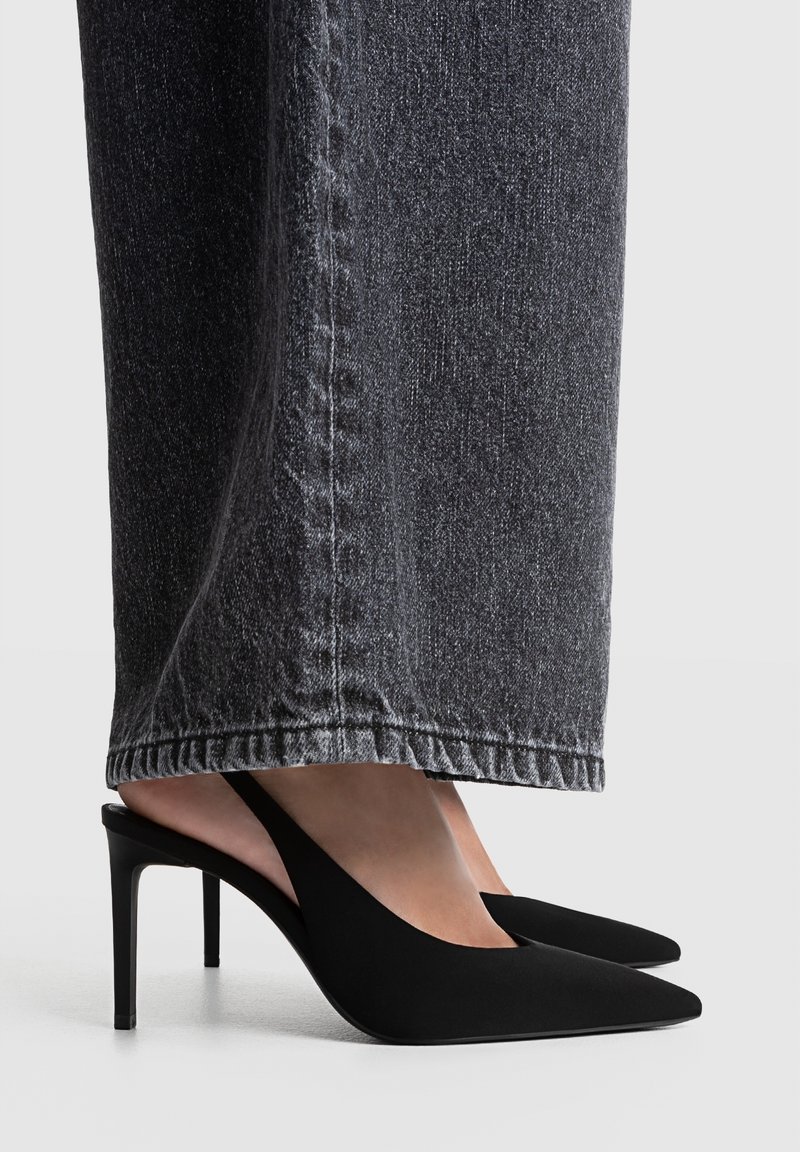 Escarpins noirs à bride arrière avec un bout pointu et une texture lisse, associés à un jean large gris foncé avec des coutures apparentes.