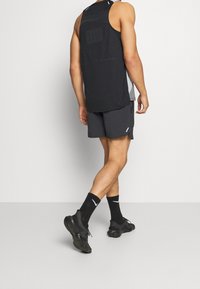 Camiseta deportiva negra sin mangas con diseño texturizado, combinada con pantalones cortos oscuros y zapatillas deportivas negras; detalles en blanco.