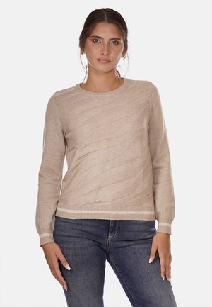 Maglione lavorato a maglia beige con un motivo a onde testurizzato, scollatura rotonda, maniche lunghe e polsini a coste, abbinato a jeans in denim scuro.