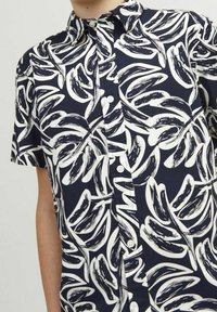 Camicia a maniche corte in tessuto blu navy con un motivo a foglie bianche, caratterizzata da un colletto button-down e bottoni frontali. Tessuto morbido, vestibilità rilassata.