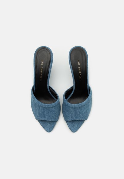Mule din denim cu toc, de culoare albastru deschis, cu vârful rotunjit și spatele deschis. Textura moale are un design pliat în față.