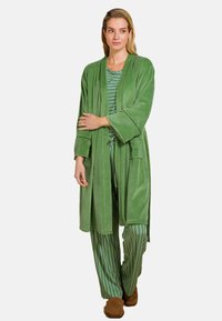 Groene, zachte stoffen badjas met lange mouwen en zakken, gedragen over een gestreept groen en wit pyjamastel. Zacht gestructureerd materiaal.