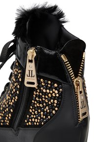 Stivale alla caviglia nero con decorazioni in metallo dorato e nero, chiusure con zip e un colletto peloso testurizzato. Realizzato in pelle verniciata.