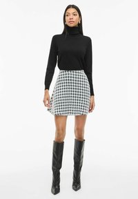 Maglione nero a collo alto abbinato a una minigonna in tessuto scozzese bianco e nero, completato da stivali al ginocchio in pelle nera.