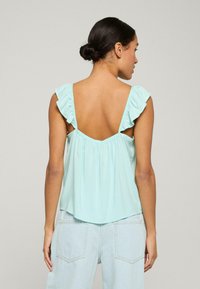 Ljust blå ärmlös topp med volangstropper, låg rygg och rynkad midja. Mjuk, slät tyg med avslappnad passform.