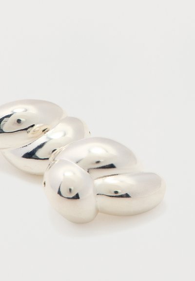 Catena di anelli in argento spessi con superfici lisce, arrotondate e riflettenti su sfondo bianco semplice.